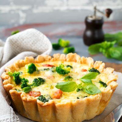 Homemade quiche tart with red fish salmon, broccoli, basil, seasonings and cheese on a gray stone ba