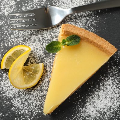 Marble tray with lemon tart slice on wooden background, top view